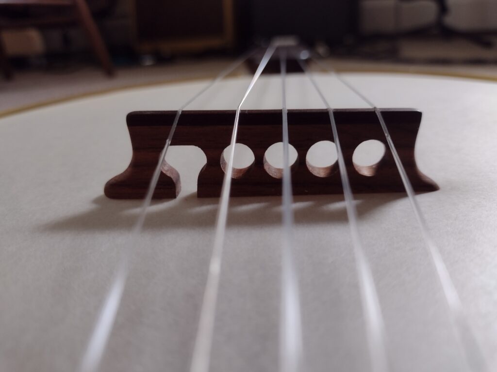 a banjo bridge with four holes and one slot under the fifth string